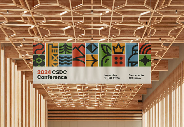 A white banner with the text CSDC 2024 Conference and colorful graphics hanging from a wooden beam ceiling