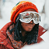 A photo of Ali, one of the personas for Powder. Ali is a female who looks to be in her twenties, and she has an orange beanie and white ski goggles on her head.