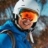 A photo of Denny, one of the personas for Powder. Denny is a male who looks to be in his thirties, and he has a white helmet and orange ski goggles on his head.